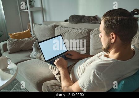 Young man using empty blank screen laptop typing and working lying on the couch at home Stock Photo