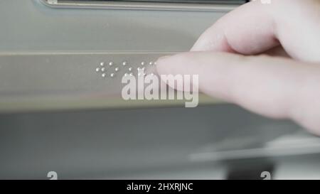 Close up of male hand touching Braille on a metal sign. HDR. Visually impaired or blind person using hand to read information on a metal sign. Stock Photo