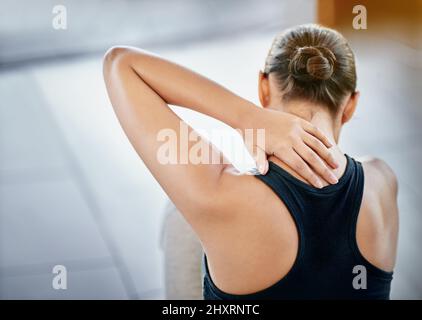 Sometimes exercise can lead to injury. Rearview shot of a young woman rubbing her neck during a workour. Stock Photo