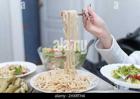 A woman puts spaghetti and fresh vegetable salad on a plate. Stock Photo