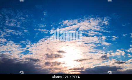 The sun sets behind a set of thick clouds with the light shining through. Stock Photo