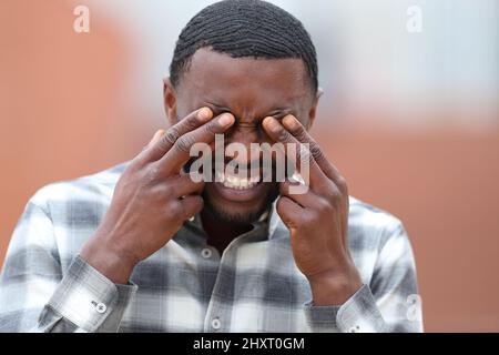 Front view portrait of a man with black skin scratching eyes in the street Stock Photo