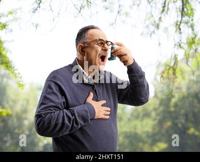 Mature man using an inhaler outdoors in a park Stock Photo