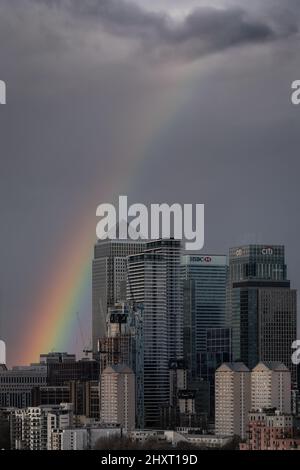 London, UK. 14th March, 2022. UK Weather: A rainbow breaks over Canary Wharf business park buildings in east London as a brief afternoon rainstorm clears. Credit: Guy Corbishley/Alamy Live News Stock Photo