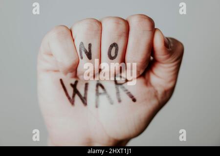 closeup of the raised fist of a man, with the text no war written in it, on a gray background Stock Photo