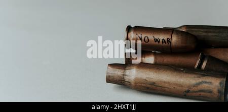 some used bullet shells on a gray background and the text no war written in a bullet on top, in a panoramic format to use as web banner or header Stock Photo