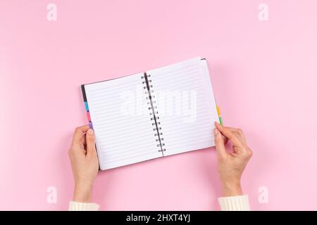 Female hands holding blank open spiral notebook on pastel pink background. Top view, copy space. Education, remote work, business, finance concept Stock Photo