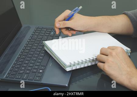 Shot of a person taking notes on a copybook, on a laptop working from home Stock Photo
