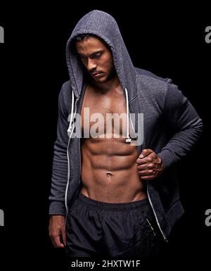 Getting his fitness on. Studio shot of a muscular young man wearing a hoodie isolated on black. Stock Photo