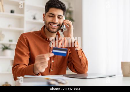 Smiling man using credit card talking on smartphone Stock Photo
