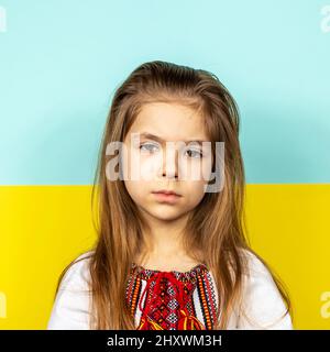 Sad girl in the national Ukrainian vyshyvanka on the background of the Ukrainian flag. Stop the war in Ukraine. The concept of peace in Ukraine Stock Photo