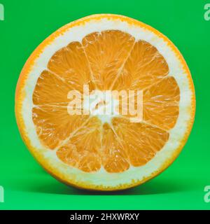 Sliced orange isolated on green background. Ripe orange citrus fruit. Stock Photo