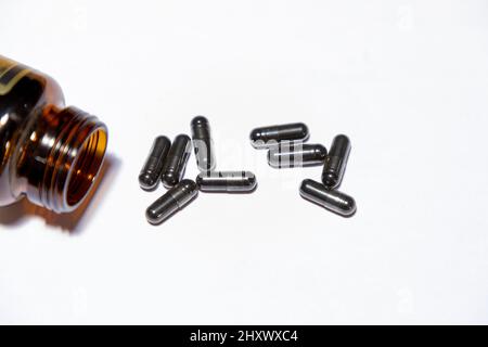 Selective focus on Black pill capsules and a bottle neck on a white background. Concept for pill addiction. Stock Photo