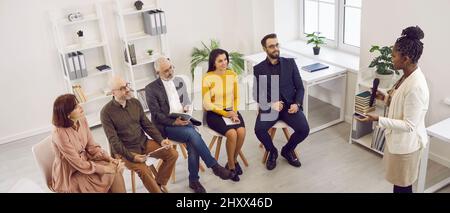Speaker talking to team of men and women who came to her business training seminar Stock Photo