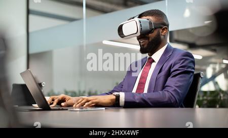 Smiling african american manager using VR glasses and laptop Stock Photo