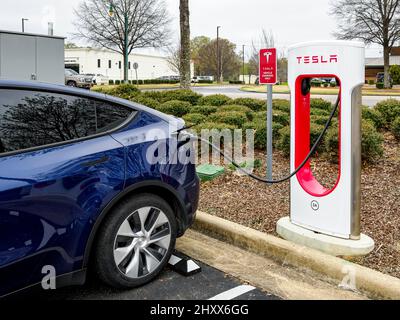 Blue Tesla Model Y, parked and charging at an electric vehicle or electric car charging station in a parking lot in Montgomery Alabama, USA. Stock Photo