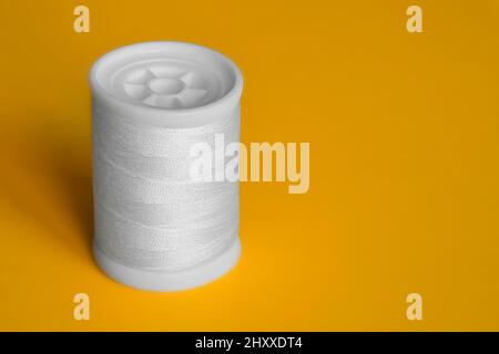 Reel of white sewing threads on yellow background. Copy space, close-up. Stock Photo