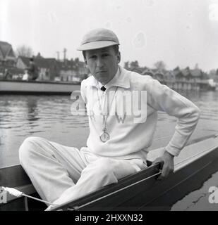 1961, historical, sitting in a rowing boat on the water, the coxswain or cox of the Cambridge University Boat team, R. T. Weston of Selwyn college, with cap and stopwatch. The initals RTW are embrodied on his cotton tracksuit top. Roger Weston had been the Cambridge cox the previous year. The Oxford & Cambridge Boat Race, the famous university rowing race, first took place 1829 and is an annaul event on the River Thames over the championship course between Putney and Barnes in South West London. Stock Photo