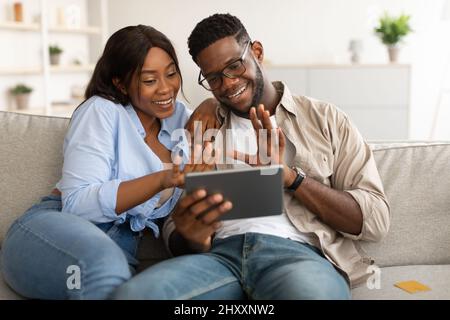 Black couple having videocall using tablet waving hands Stock Photo
