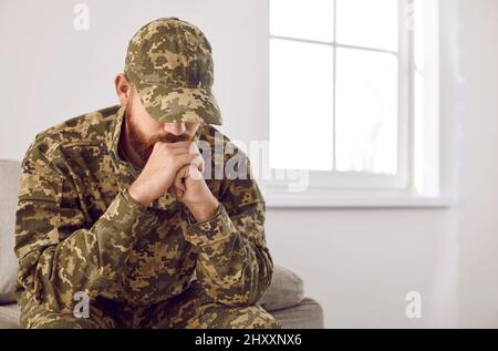 Depressed unhappy veteran soldier with PTSD sitting on sofa and thinking about war Stock Photo