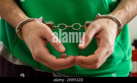 Arrest, Handcuffed criminal man hands close up. Hand cuffs locked in front, protection from crime and law violation. Stock Photo