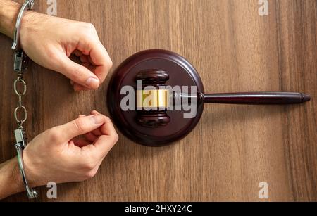 Handcuffed Convict, Law offender and Justice. Court sentence Prison. Handcuff locked and judge gavel on a wooden table, top view. Stock Photo