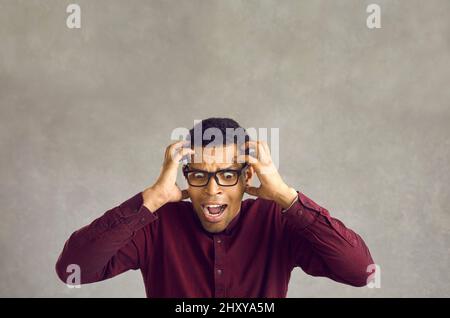 Portrait of scared desperate young black man holding his head and screaming in panic Stock Photo