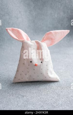 Bag of sweets in shape of Easter bunny with ears on light gray background. Packing made of cotton fabric in form of cute bunny or rabbit, sewing for Stock Photo