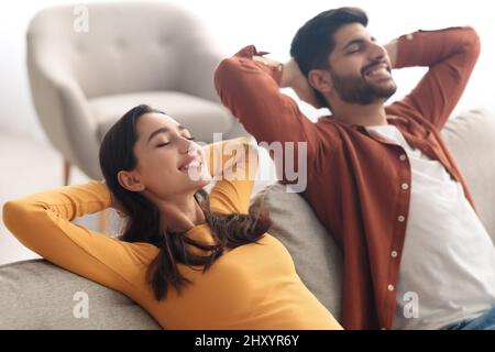 Relaxed Middle Eastern Spouses Sitting On Sofa Relaxing At Home Stock Photo