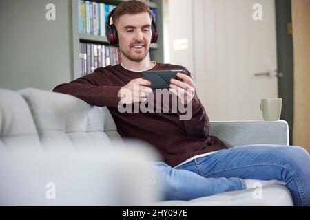 Man At Home Wearing Wireless Headphones Streaming Music Or Film From Mobile Phone Stock Photo