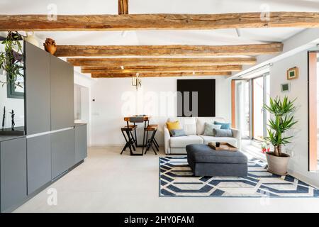 Living room with gray sideboard, exit to a terrace, sofas and old wooden beams on the ceiling Stock Photo