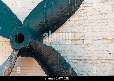 Close-up shot of an old propeller of the engine of the ship by the white brick wall outdoors Stock Photo