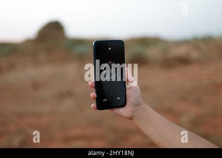 Crop anonymous female traveler using compass on modern smartphone to orientate while standing in desert area during trip in nature Stock Photo