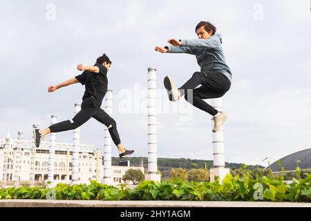 Side view of full body strong parkour athletes in sportswear doing jump exercise on street against building Stock Photo