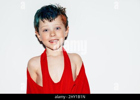 Mischievous boy with colorful dyed hair grinning and showing teeth while looking at camera on white background in light room Stock Photo