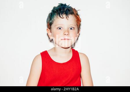 Mischievous boy with colorful dyed hair grinning and looking at camera on white background in light room Stock Photo