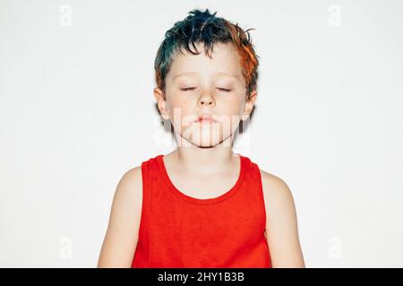 Mischievous boy with colorful dyed hair and closed eyes on white background in light room Stock Photo