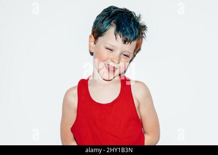 Mischievous boy with colorful dyed hair grinning and showing teeth while looking away on white background in light room Stock Photo