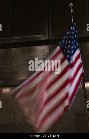 Colorful blurred national American flag with stars and stripes in motion hanging on dark street near wall in night time Stock Photo