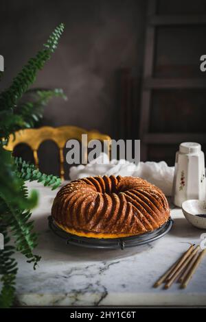 Delicious homemade cake with poppy seeds placed near candles and green plant in kitchen at home on blurred background Stock Photo