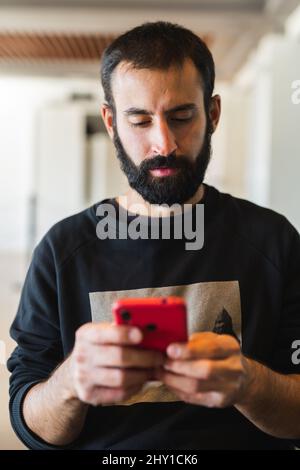 Adult male with beard wearing casual long sleeve shirt texting message on modern cellphone Stock Photo