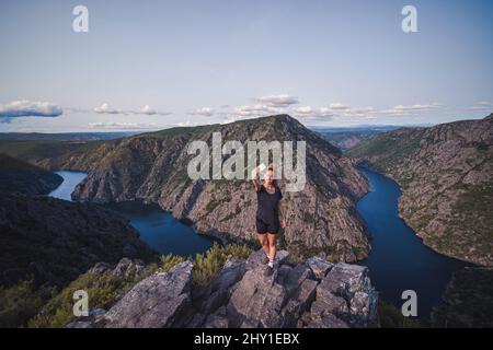 From above of full lenght adult female tourist in sportswear standing on top and taking selfie on smartphone while enjoying picturesque landscape Stock Photo