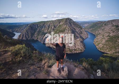 From above of full lenght adult female tourist in sportswear standing on top and taking selfie on smartphone while enjoying picturesque landscape Stock Photo