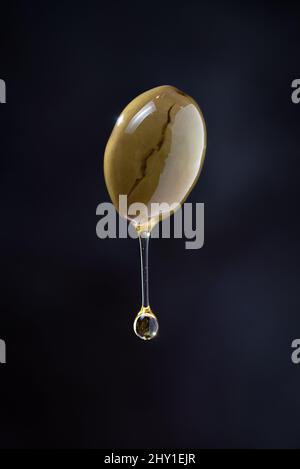 Thin stream of olive oil dripping from square piece of falling dough with drop on black background in modern studio Stock Photo