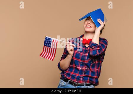Funny woman peeks out from behind open notebook, holds copybook over head. Student girl shows USA flag and workbook. Study abroad. International student exchange program. Learning American English Stock Photo