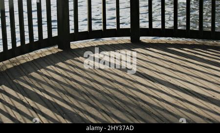 Lines of shadows on wooden decking late in the afternoon, with wooden fence around a lake, taken in winter time Stock Photo