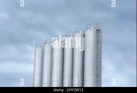 Stainless steel milk tanks at a  modern dairy farm. Large storage tanks used in the beverage industry against a cloudy sky. Stock Photo