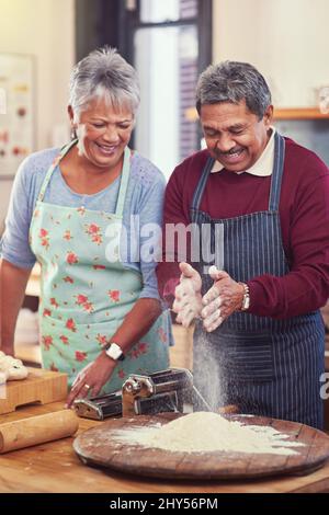 When preparing food ones hands might get dirty. Shot of a happy mature couple having fun together while preparing pasta from scratch at their home. Stock Photo