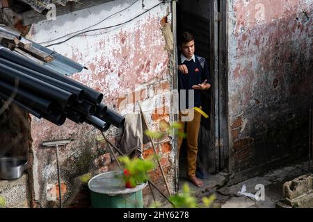 Young Cuban man wearing his school uniform stands in the doorway of his house checking out the gentle rain falling from the clouds. Stock Photo