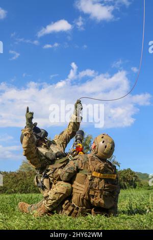 Hawaii Army National Guard (HIARNG) Soldier, Sgt. 1st Class Matthew Mitsui, (left) a flight paramedic with Detachment 1, Golf Company, 1st Battalion, 189th Aviation Regiment, signals the aircraft as they prepare to lift a simulated patient during medevac helicopter hoist training with the 31st Marine Expeditionary Unit’s (MEU) Maritime Raid Force at Marine Corps Training Area Bellows (MCTAB) at Bellows, Hawaii, Jan. 5, 2022. This training assisted Soldiers with certifying their special skills while performing multiple medevac procedures during an air rescue emergency situation. (U.S. Army Nati Stock Photo